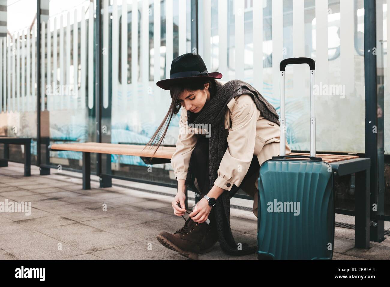 Giovane ragazza turistica stringe scarpe mentre siede a una fermata dei mezzi pubblici Foto Stock