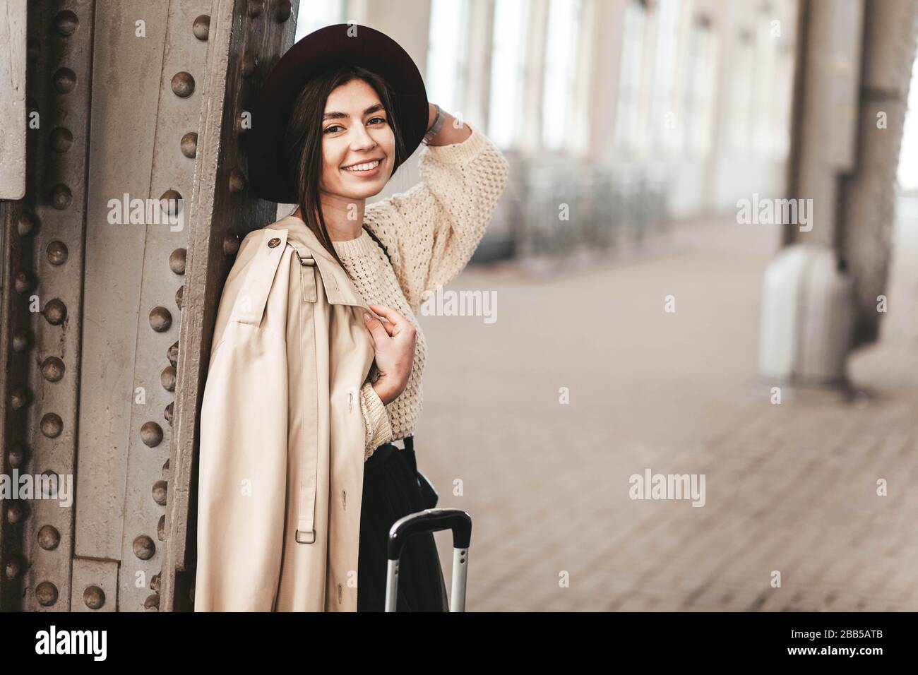 Ritratto di giovane donna bella viaggiatore in casual cappotto e cappello che è in attesa di un treno sulla piattaforma della stazione ferroviaria Foto Stock