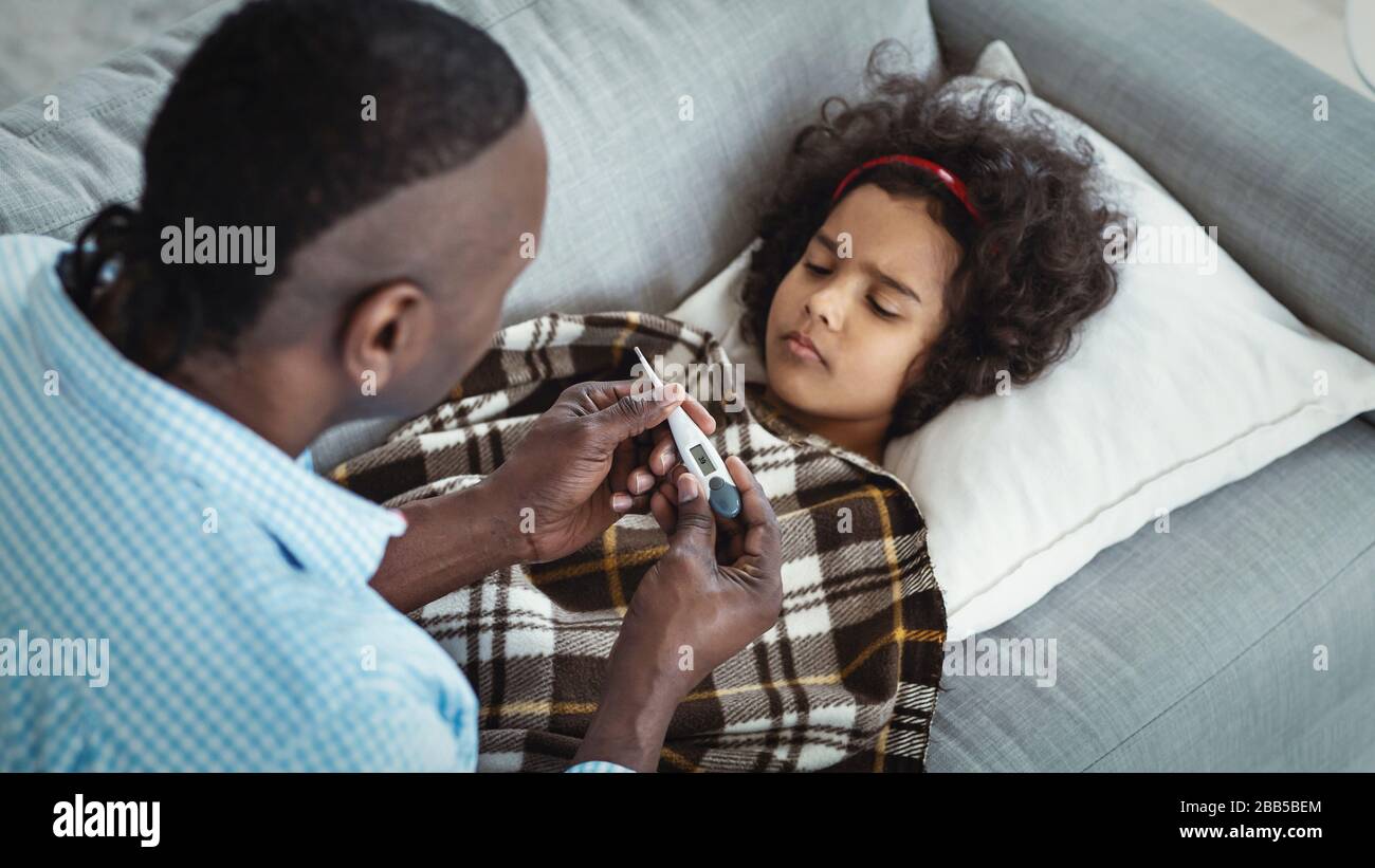 Pandemia mondiale. Adorabile ragazza afroamericana con febbre alta e nonno che si prende cura di lei a casa Foto Stock