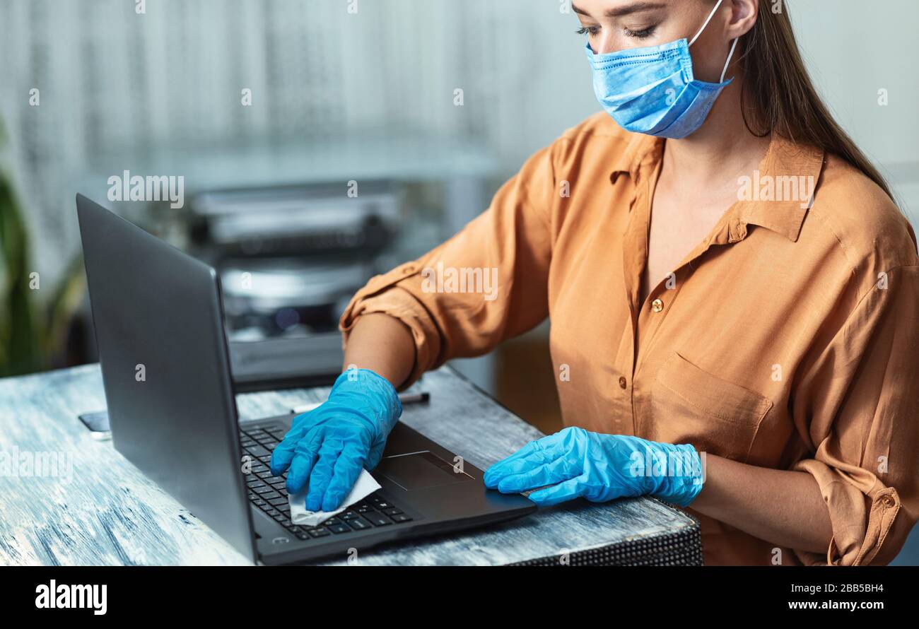 Donna in quarantena indossando guanti per la pulizia della tastiera del computer portatile Foto Stock