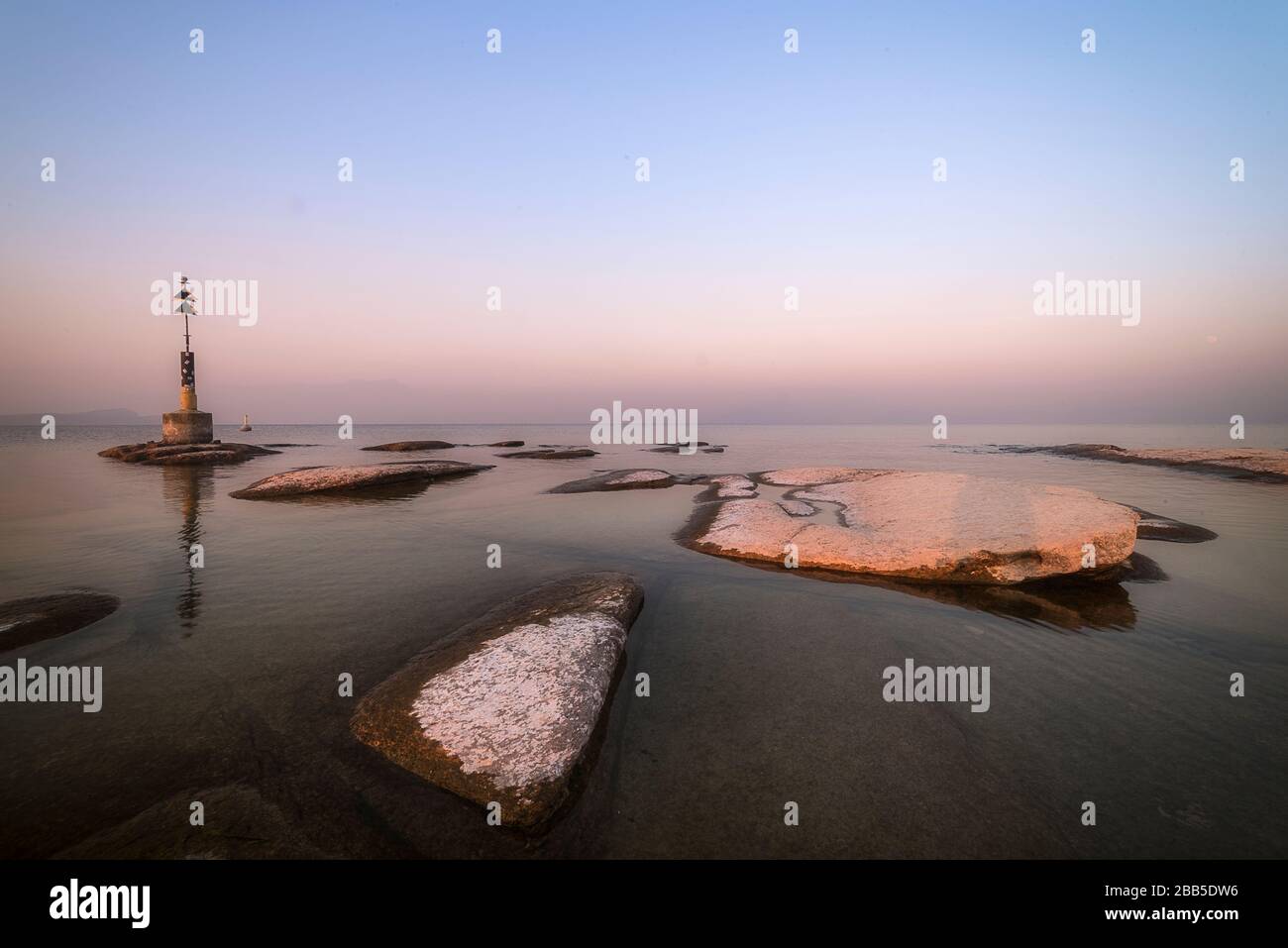 spiaggia di sirmione di notte e tramonto sul lago di Garda con rocce piatte sulla spiaggia e acqua e sole in l'orizzonte Foto Stock
