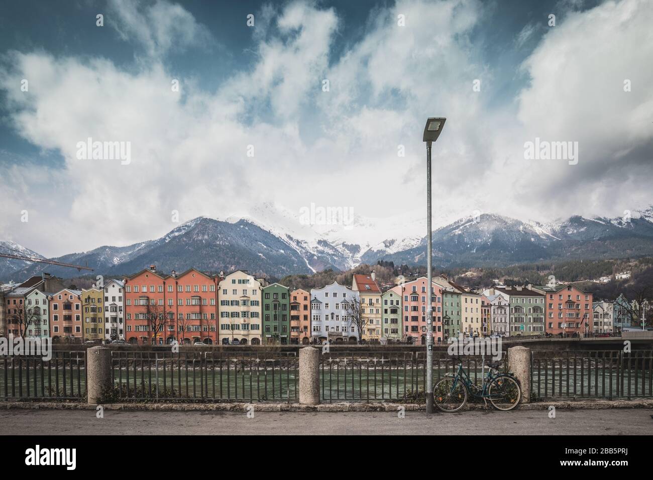 Vista sul centro storico di Innsbruck, con case colorate lungo il fiume Inn e famose vette di montagna austriache sullo sfondo con una bicicletta, Foto Stock