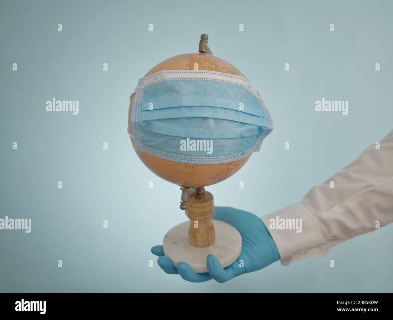 Global Pandemic Covid-19 Coronavirus, braccio del medico che tiene il globo con maschera chirurgica blu. Studio shot, braccio estensibile con mano guanto da laboratorio Foto Stock