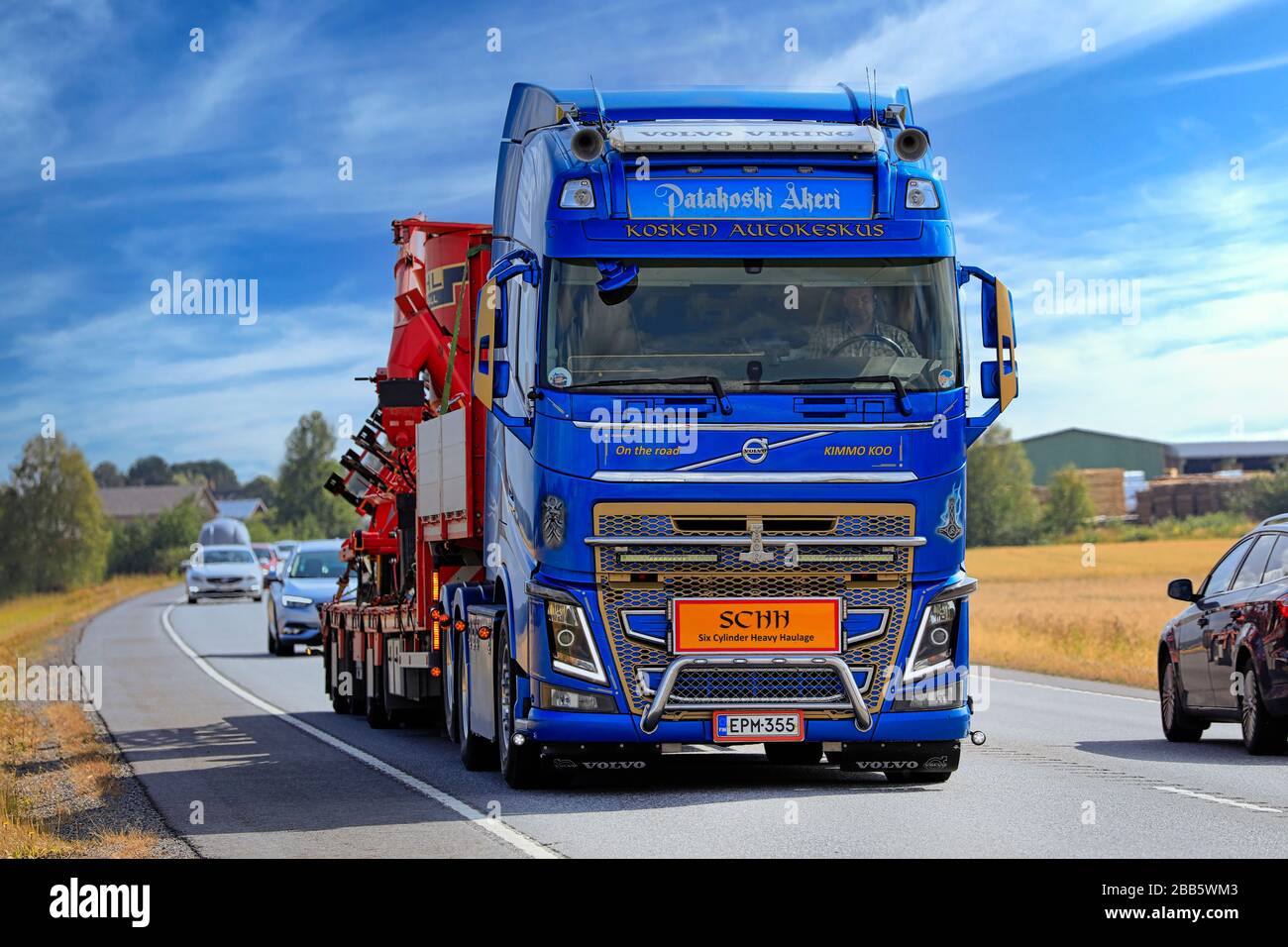 Blue Volvo FH Viking di Patakoski Akeri trasporta macchinari agricoli nel traffico autostradale in una giornata di sole. Luopajarvi, Finlandia. 8 agosto 2019. Foto Stock