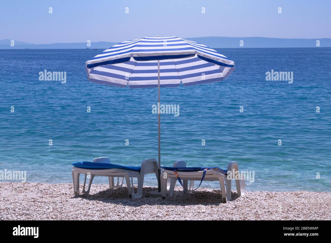 Ombrellone blu e chaise per il relax e la comodità sul mare resort. Vacanze estive e viaggi per mare. Servizio a pagamento sul litorale confortevole. Foto Stock
