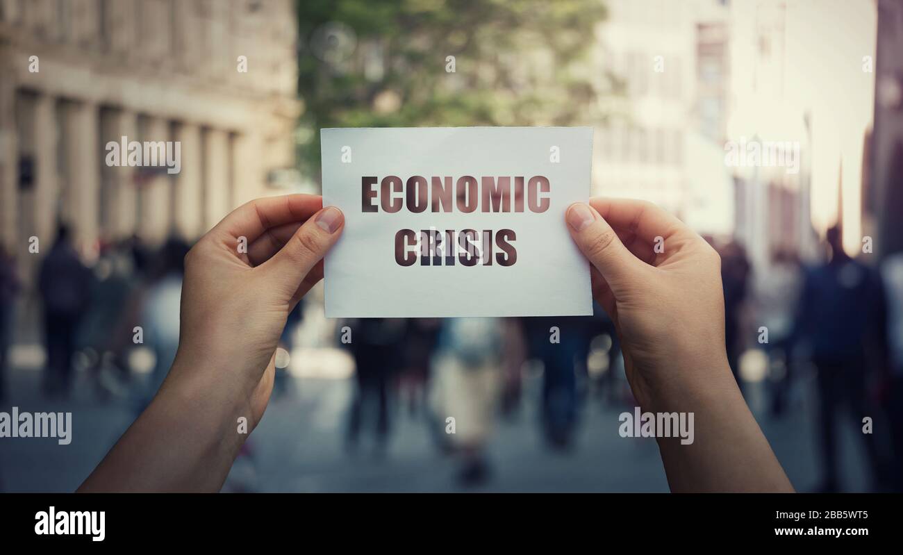 Mani che tengono un foglio di carta di avvertimento circa il concetto di crisi economica globale su un fondo stradale affollato. Recessione mondiale, collasso economico dovuto t Foto Stock