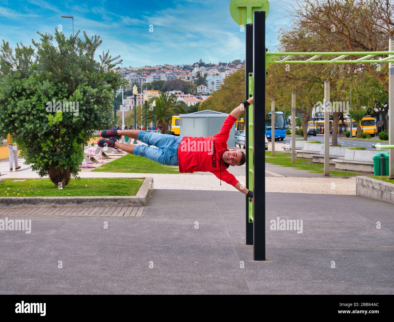 Un giovane uomo in forma mostra la sua forza con una bandiera umana tenere sulle barre di muro in piedi libera in un parco pubblico a Funchal, Madeira in una giornata di sole. Foto Stock
