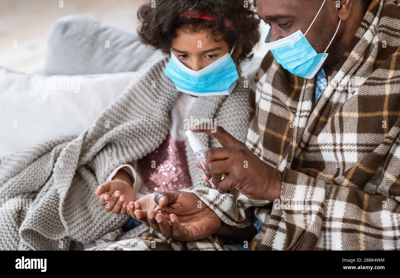 Igiene delle mani durante la pandemia. Uomo e nipote afroamericani con maschere che applicano antisettico a casa Foto Stock