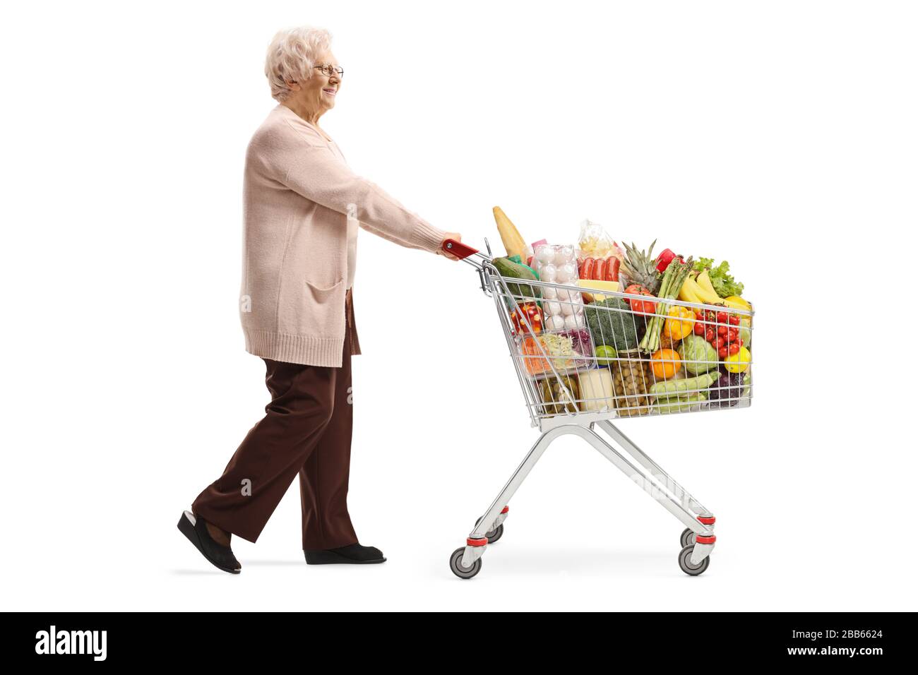 Profilo a tutta lunghezza di una donna anziana che spinge un carrello pieno di cibo isolato su sfondo bianco Foto Stock