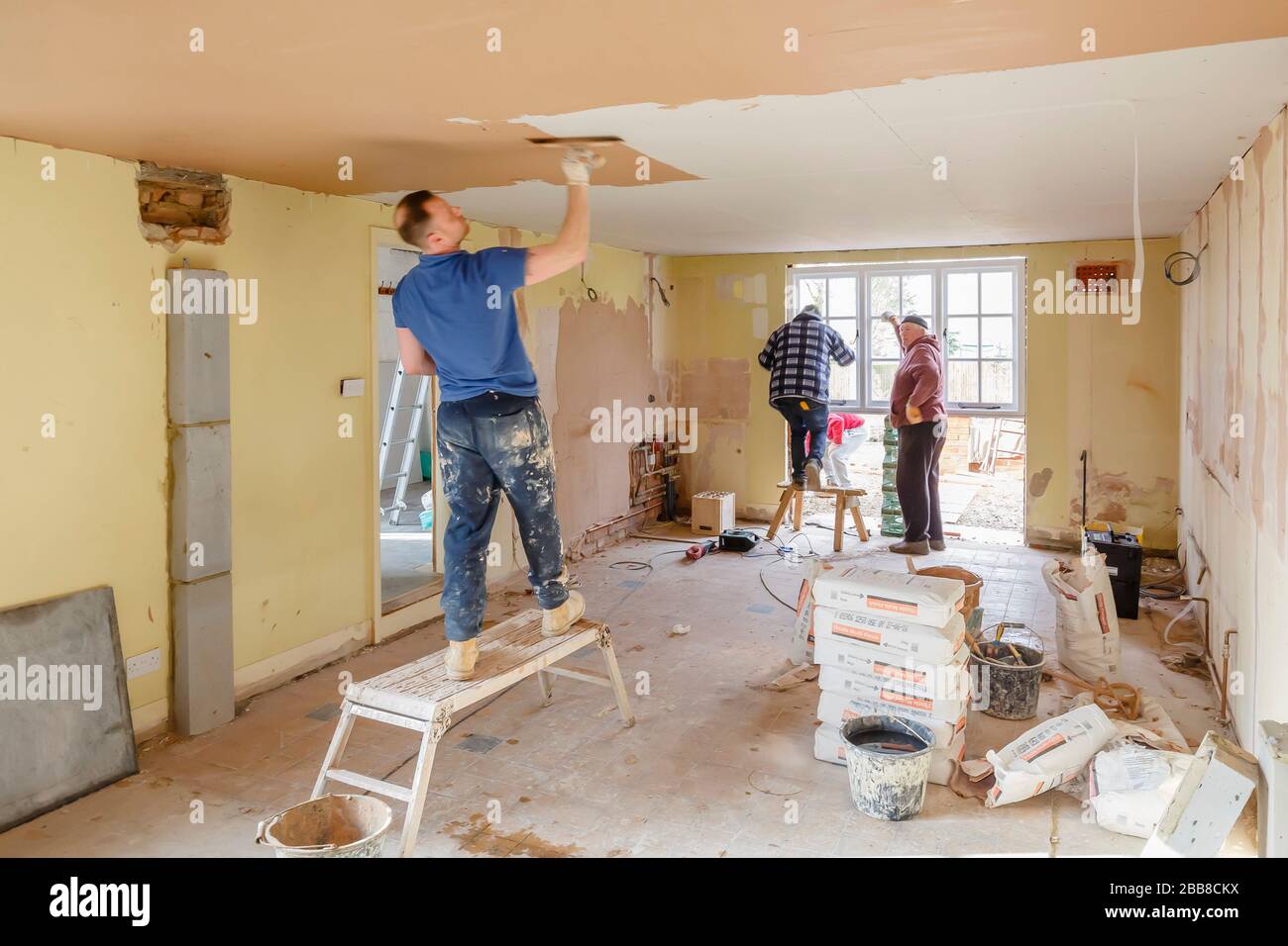 BUCKINGHAM, Regno Unito - 14 marzo 2016. Team di costruttori che lavorano per una casa di ristrutturazione degli interni con intonaco intonaco che rasa un nuovo soffitto Foto Stock