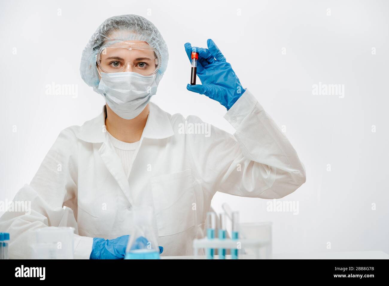 medico in uniforme protettiva con maschera contenente campione di sangue con coronavirus Foto Stock