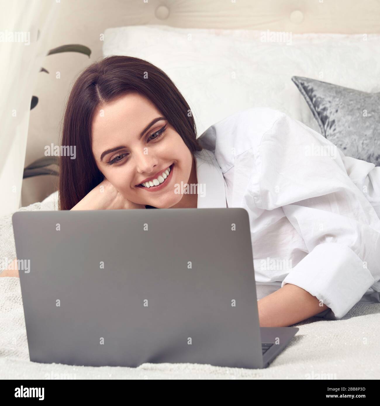 Felice ragazza sorridente usando il portatile e sorridente nel suo letto Foto Stock