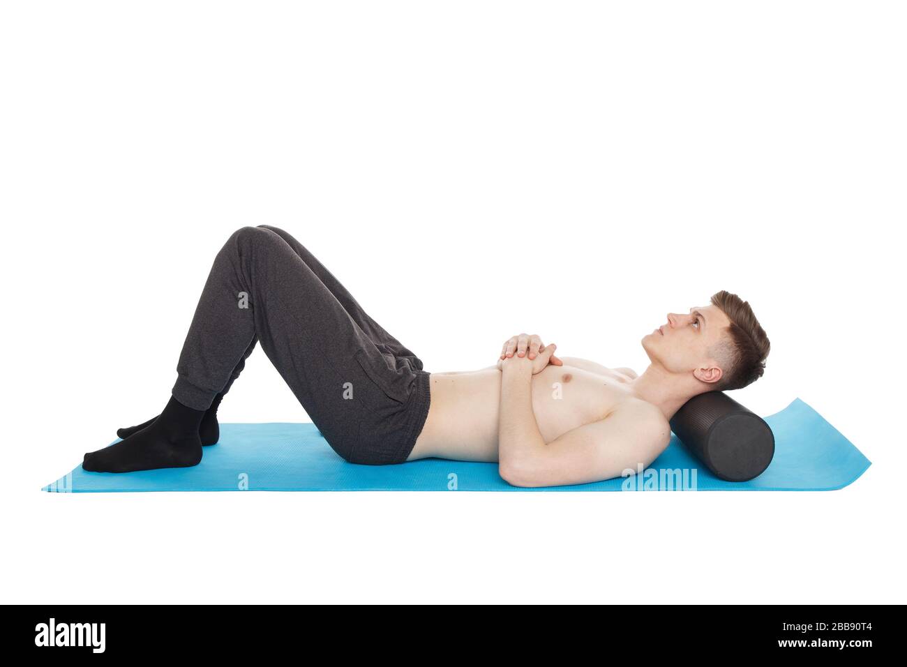 Il bell'uomo mostra esercizi, utilizzando un rullo in schiuma per un massaggio miofasciale sul tappetino da ginnastica in studio. Isolato su bianco. Foto Stock