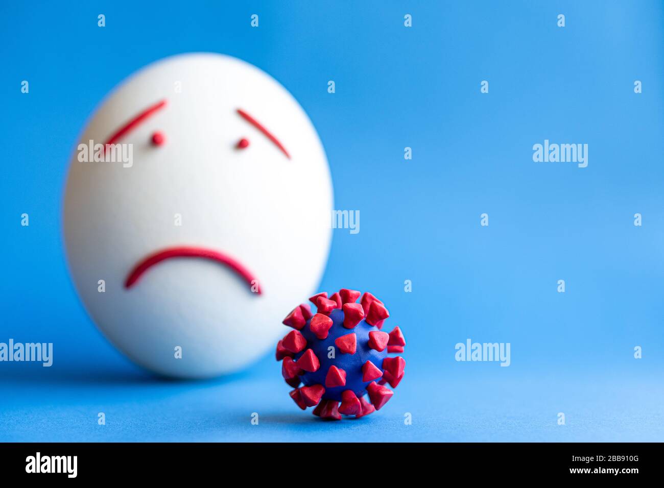 Modello di coronavirus plastificato e isolato di uovo su sfondo blu. Modello plastilina di coronavirus e uovo di pasqua raffigurante paura e tristezza. Grande Foto Stock