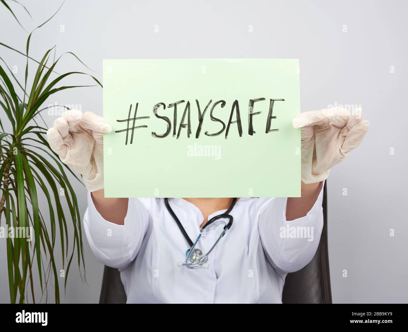 giovane donna medico in un cappotto bianco, guanti medici sterili tiene un poster con l'iscrizione stare al sicuro, concetto di auto-isolamento durante una pandemia Foto Stock