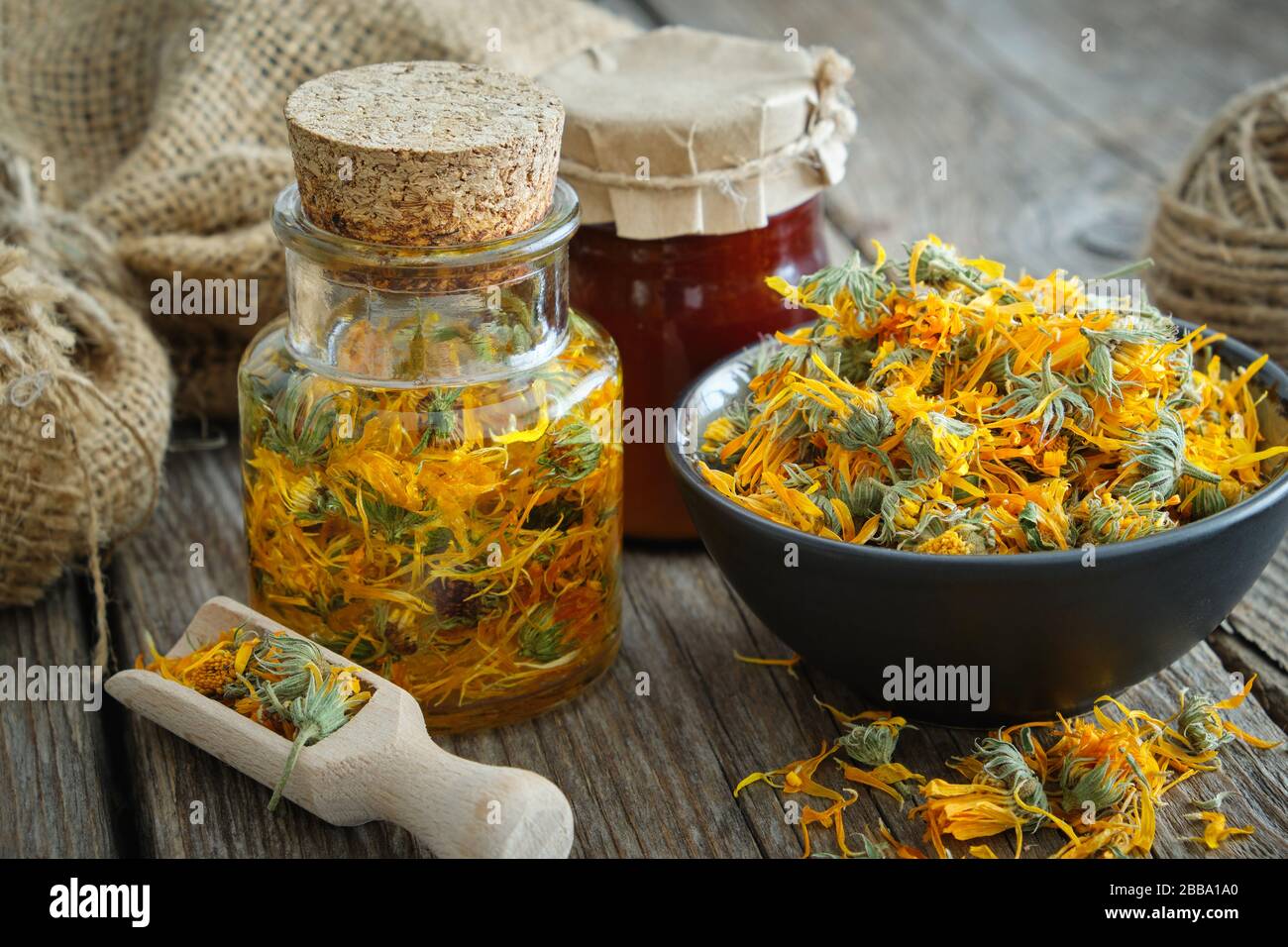 Bottiglie di calendula infusione o olio, fiori marigold sani in ciotola e calendula salve su tavolo di legno. Medicina di erbe. Foto Stock