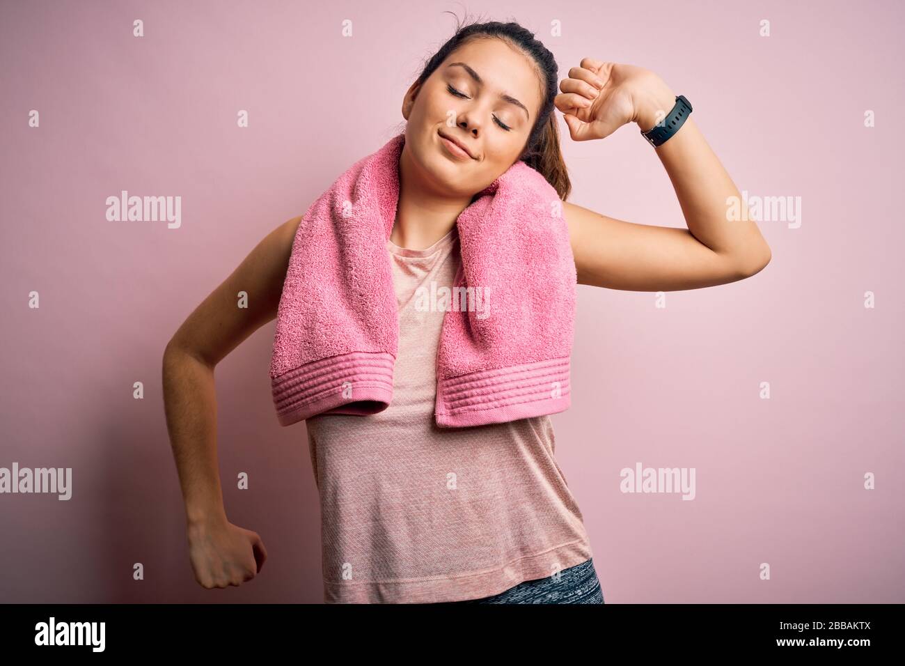 Giovane bella bruna sportswoman indossare abbigliamento sportivo e asciugamano su sfondo rosa che si allunga indietro, stanco e rilassato, assonnato e tendente per earl Foto Stock