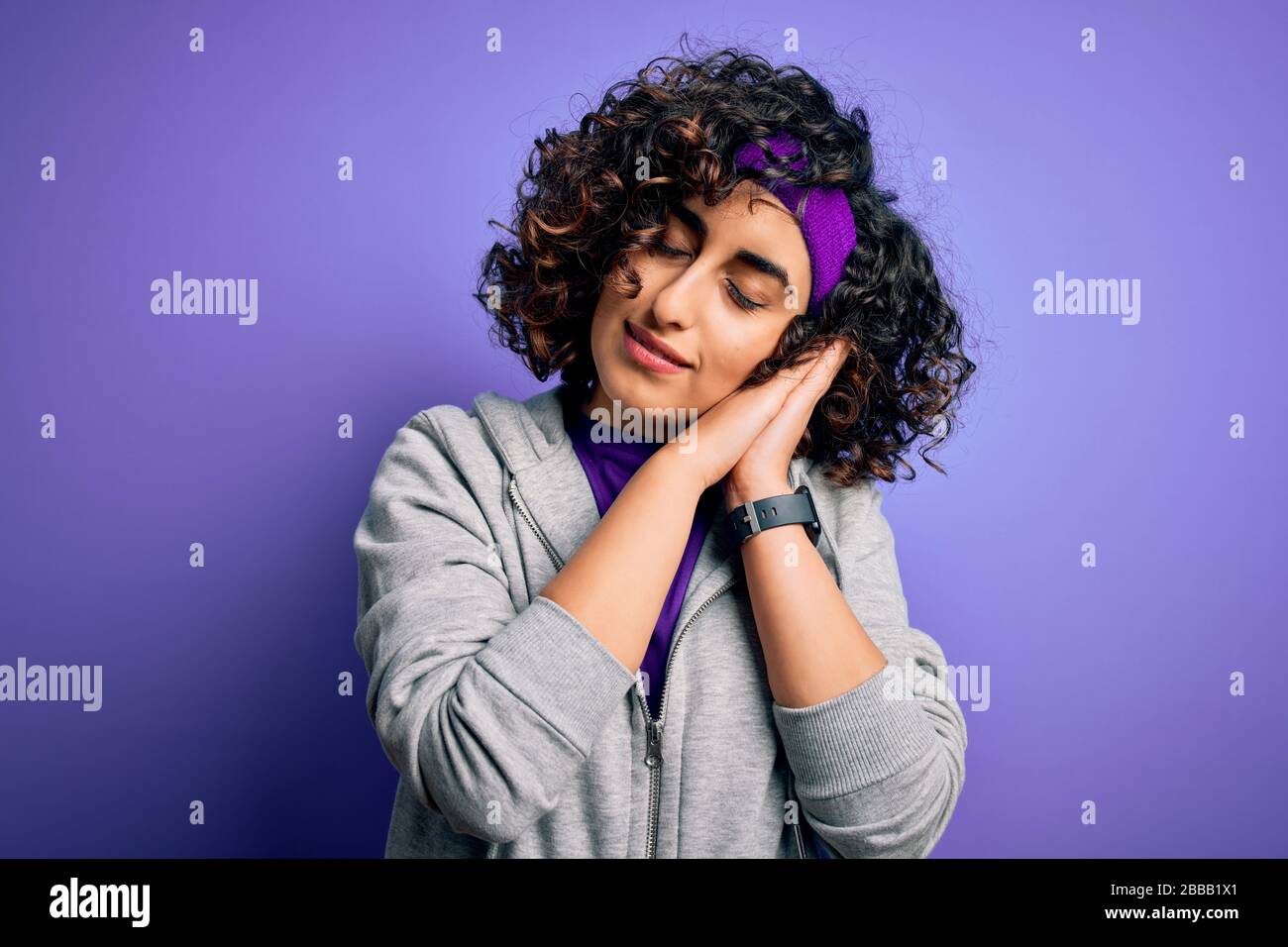 Bella curly arab sportswoman fare sport indossando abbigliamento sportivo su sfondo viola dormire stanco sognare e posare con le mani insieme, mentre mq Foto Stock