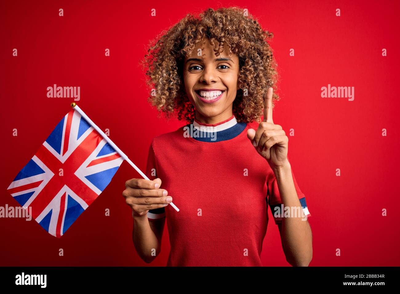 La giovane donna maledetta afroamericana che tiene la bandiera britannica per celebrare il referendum sulla brexit ha sorpreso con un’idea o una domanda che punta il dito con il volto felice, n Foto Stock