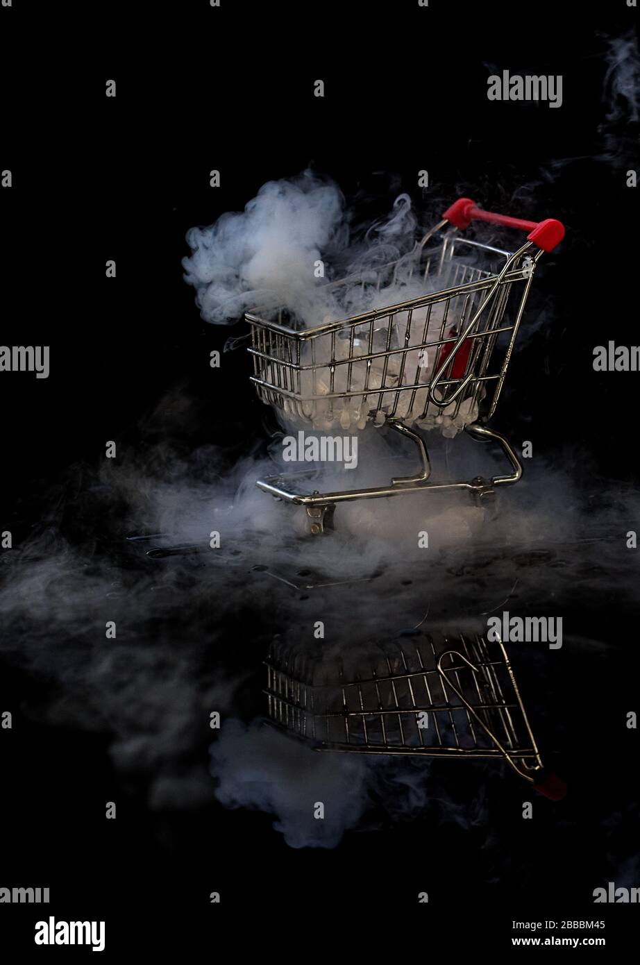 Carrello per lo shopping con fumo di ghiaccio secco e riflessi su sfondo nero Foto Stock