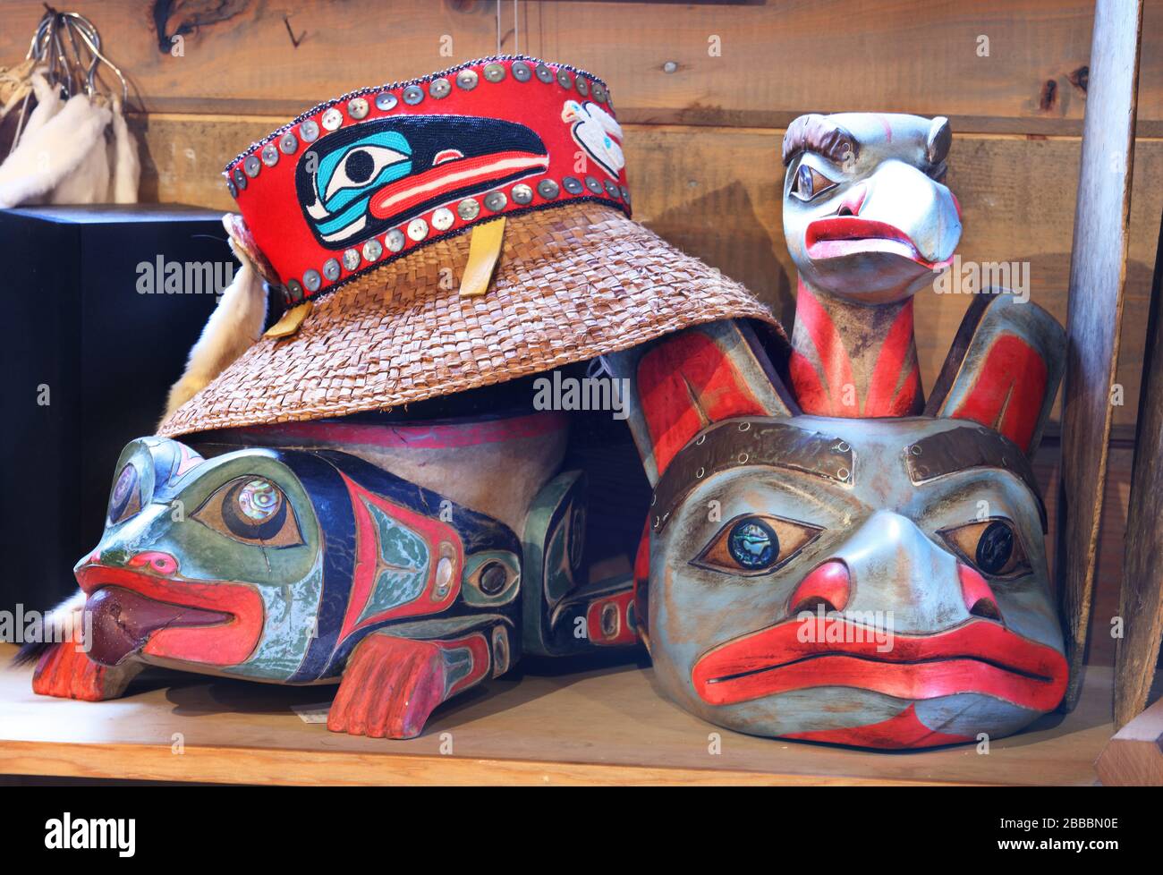 Cappello di paglia in stile Haida sulla parte superiore di una maschera frontale di rana ispirata a Tlingi. A destra c'è una maschera frontale d'orso ispirata a Tlingit nel negozio d'arte nativo Deil'e.ann & Tlingit Botanicals, Icy Strait Point, Alaska, U.S.A. Foto Stock