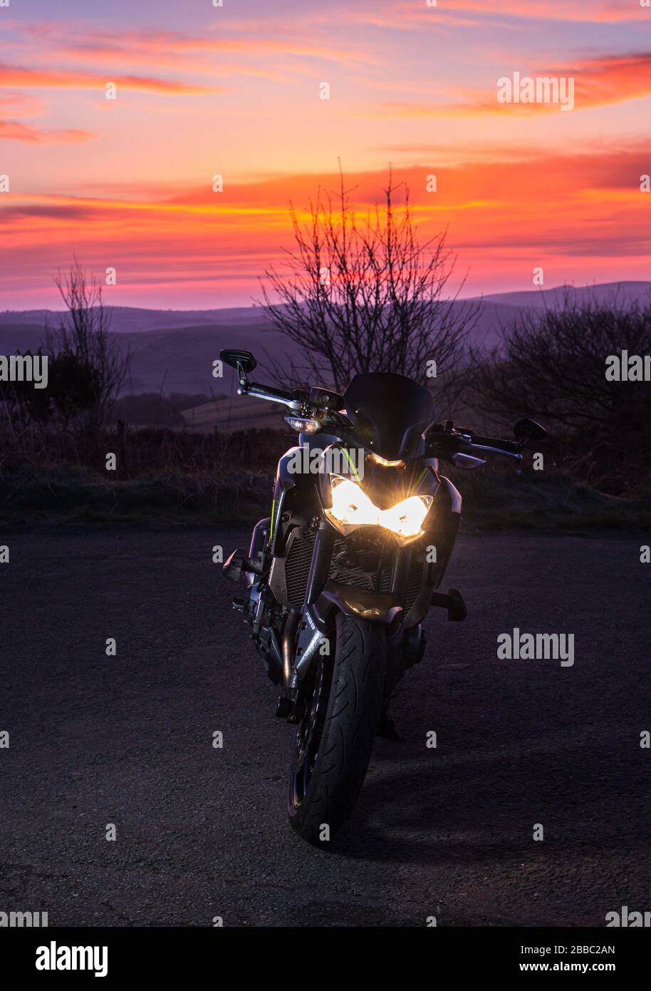 Moderna moto sportiva parcheggiata a scenografica loacation rurale con Vvid rosso crepuscolo cielo - paesaggio raccolto Foto Stock