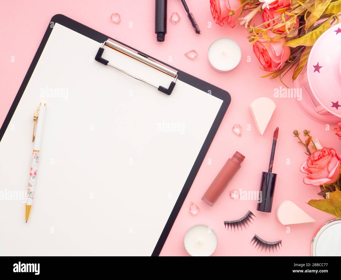 Appunti e strumenti di trucco e prodotti cosmetici e fiori di rose intorno ad esso isolato su uno sfondo di colore rosa. Disposizione piatta, spazio copia vista dall'alto. Femin Foto Stock