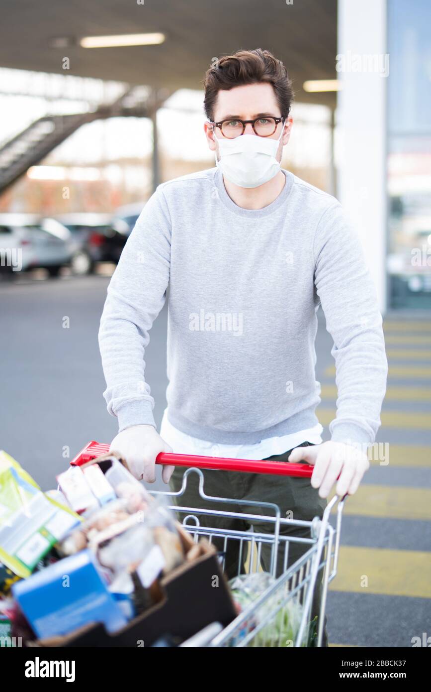 Uomo con maschera respiratoria e guanti in gomma di fronte a un supermercato Foto Stock