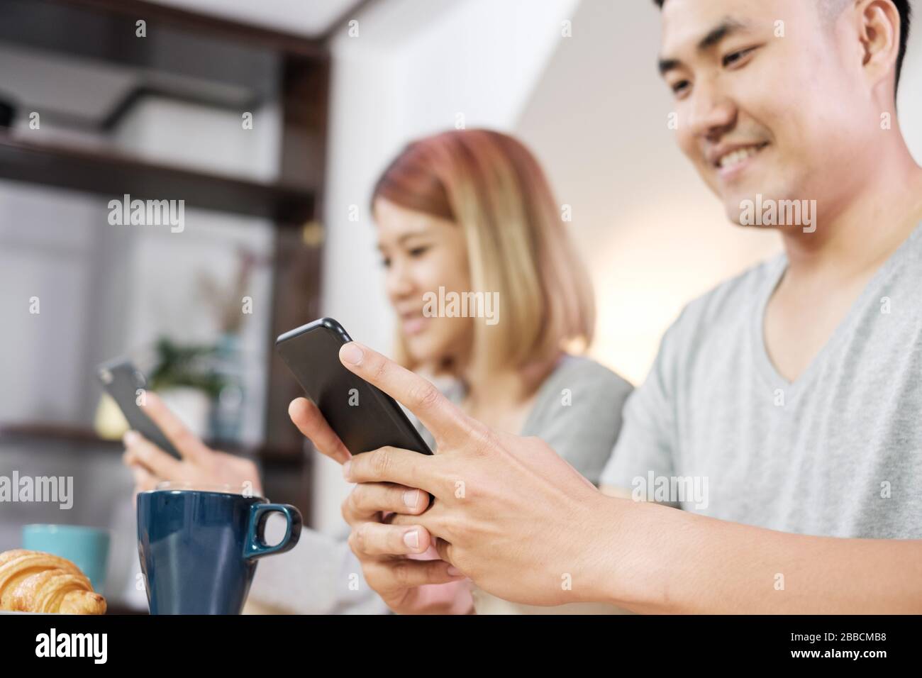 felice coppia asiatica in pigiama seduto al tavolo in cucina e guardare il video sul dispositivo mobile di togerther a casa al mattino e di avere cereale breakfast.focus Foto Stock