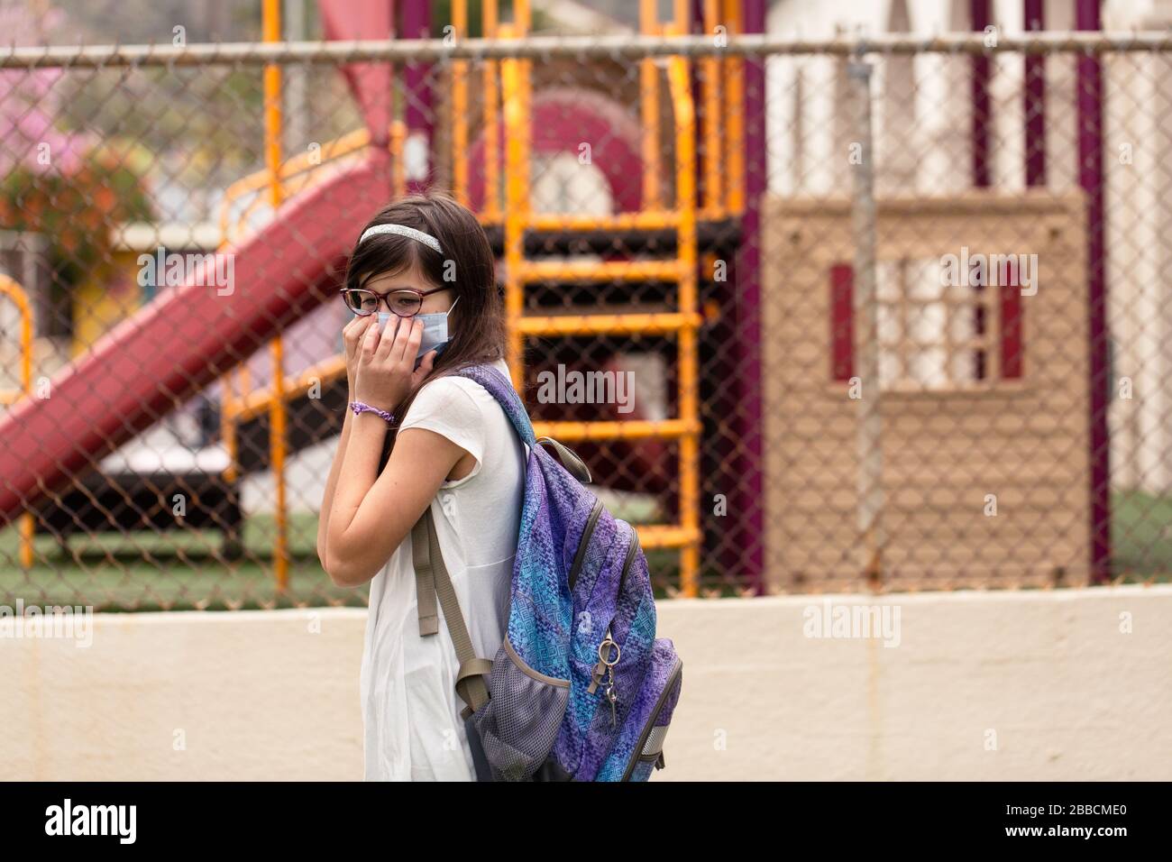 Una ragazza è preoccupata che la sua scuola sia chiusa. Lei è desiderosa di assistere con una maschera di faccia sopra. Foto Stock