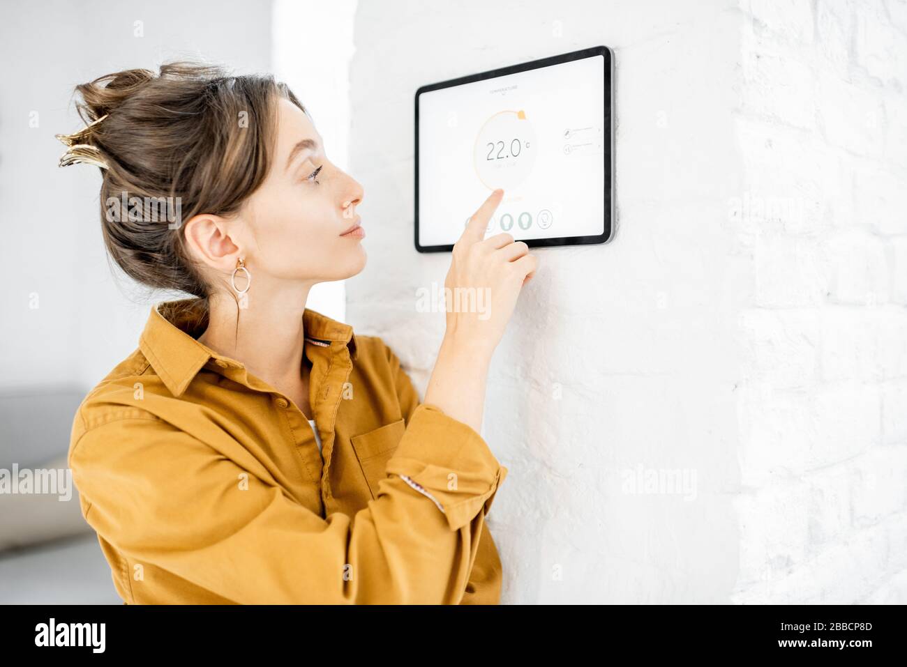 Giovane donna che controlla la temperatura nel soggiorno con un pannello touch screen digitale. Concetto di controllo del riscaldamento in una casa intelligente Foto Stock