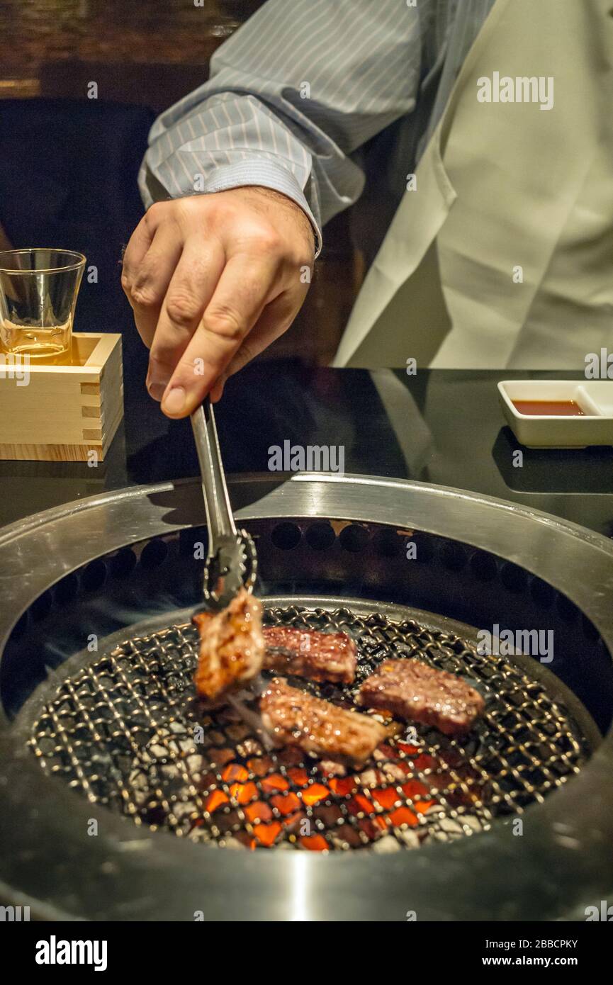 Uomo grigliando pezzi di manzo su una griglia da tavolo in un ristorante coreano barbecue, Tokyo, Giappone Foto Stock