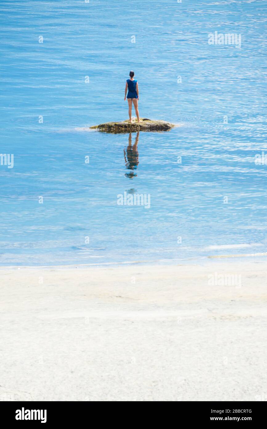 Una giovane donna posa su una roccia di fronte ad una spiaggia sull'Isola Savary, British Columbia Foto Stock