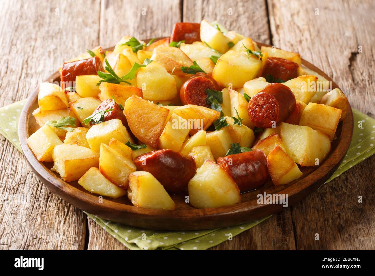 Ricetta di patate fritte con salsicce speziate e prezzemolo fresco primo piano in un piatto sul tavolo. Orizzontale Foto Stock