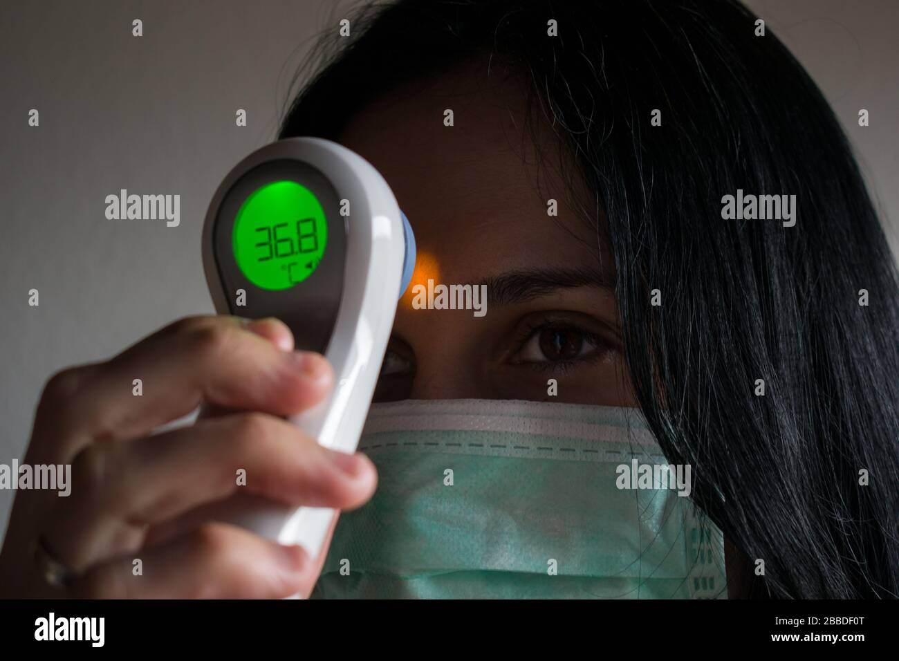 Giovane donna con maschera medica protettiva che misura la temperatura, primo piano Foto Stock