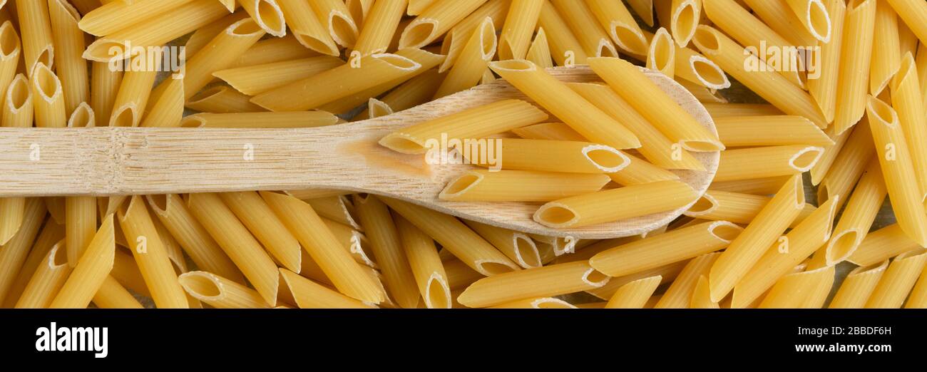 Sfondo alimentare - Penne secca pasta e cucchiaio di legno, integrale di grano crudo ingrediente Foto Stock