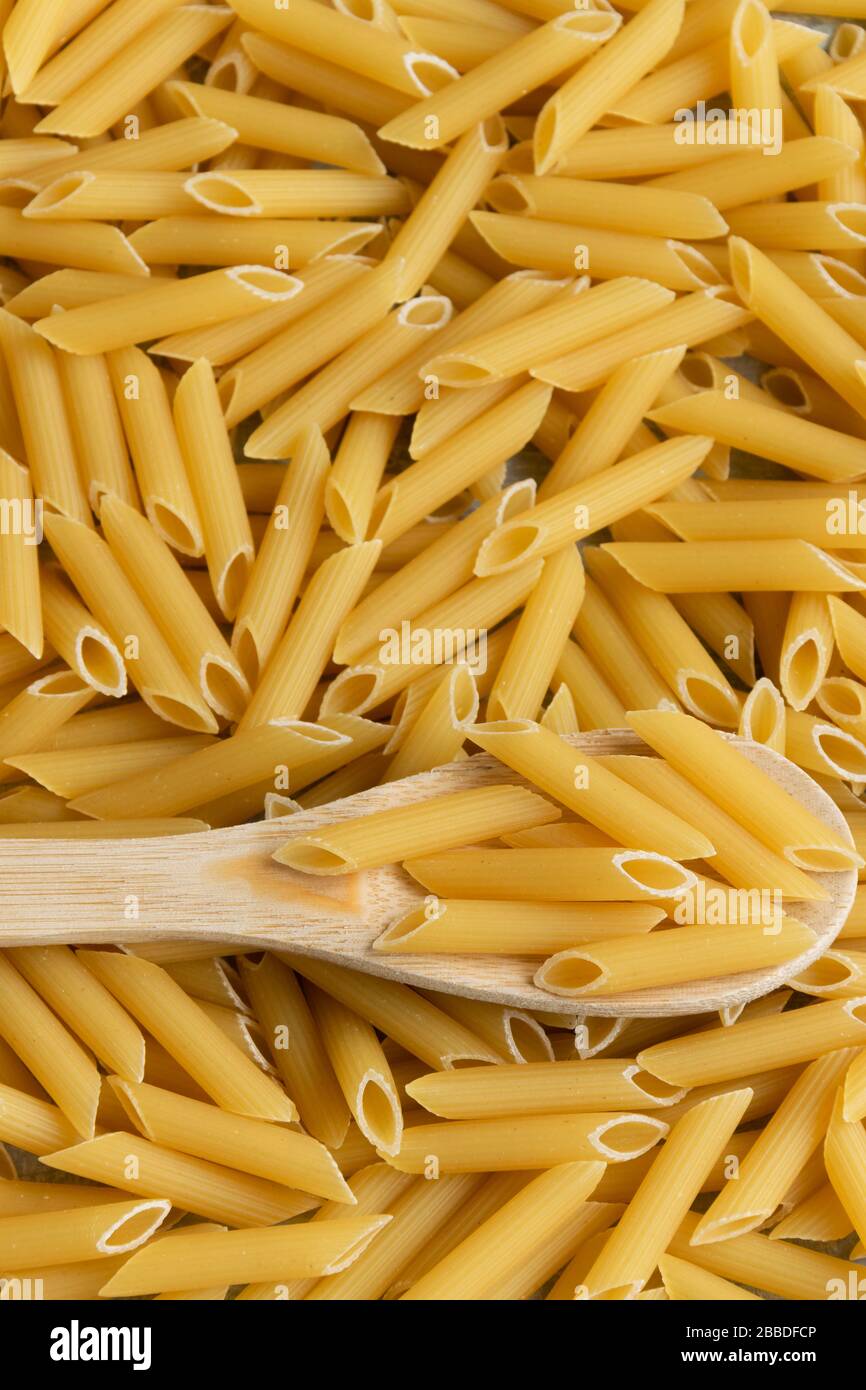 Sfondo alimentare - Penne secca pasta e cucchiaio di legno, integrale di grano crudo ingrediente Foto Stock