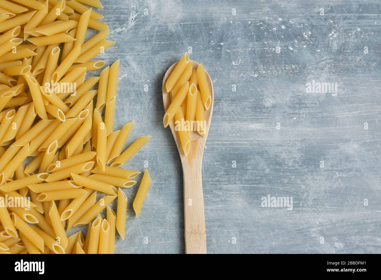 Food background - pasta secca penne e cucchiaio di legno, integrale grano crudo ingrediente, spazio per il testo Foto Stock