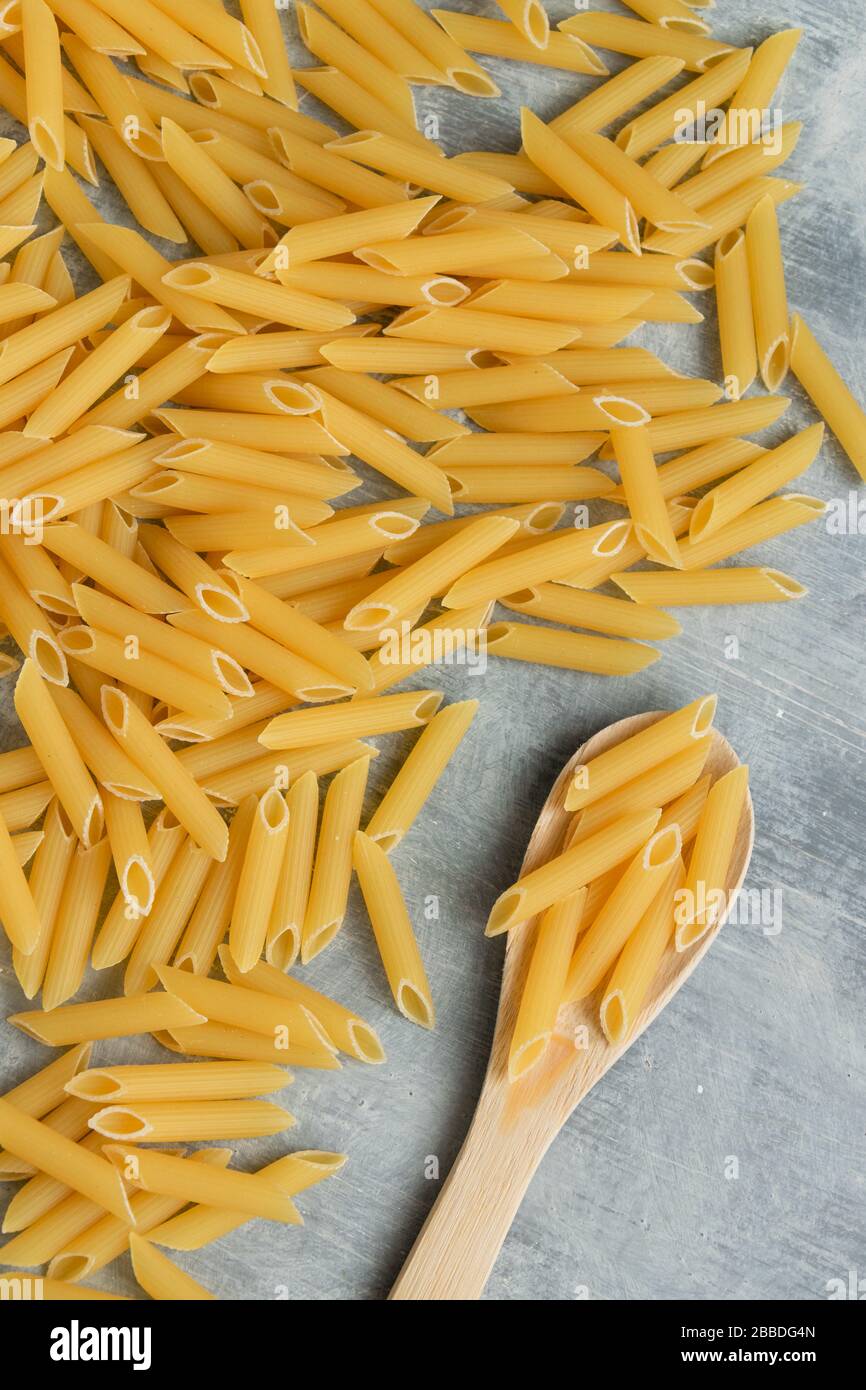 Food background - pasta secca penne e cucchiaio di legno, integrale grano crudo ingrediente, spazio per il testo Foto Stock