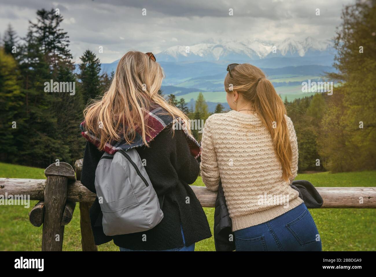 Foto dalla parte posteriore di due giovani donne vicino alla recinzione in legno su pittoresco sfondo di paesaggio di montagna, Polonia, Tatra Foto Stock