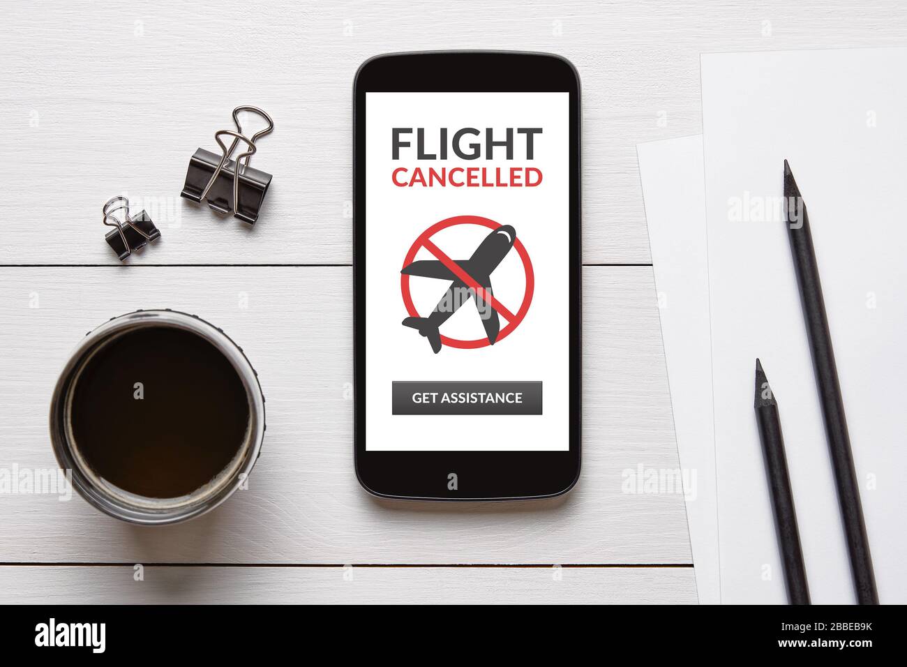 Concetto di volo annullato sullo schermo dello smartphone con oggetti da ufficio sul tavolo in legno bianco. Vista dall'alto Foto Stock