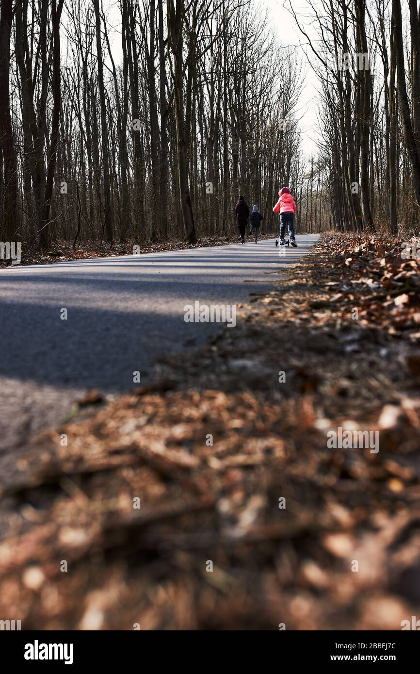 Ragazza in sella a uno scooter su strada nel parco. Famiglia trascorrere il tempo insieme all'aperto. Persone reali, situazioni autentiche Foto Stock