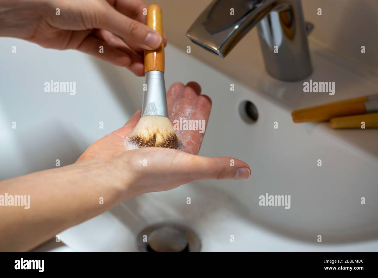Le mani delle donne che lavano le spazzole eco-friendly di trucco con i manici di bambù con sapone e acqua. Cura igienica. Foto Stock