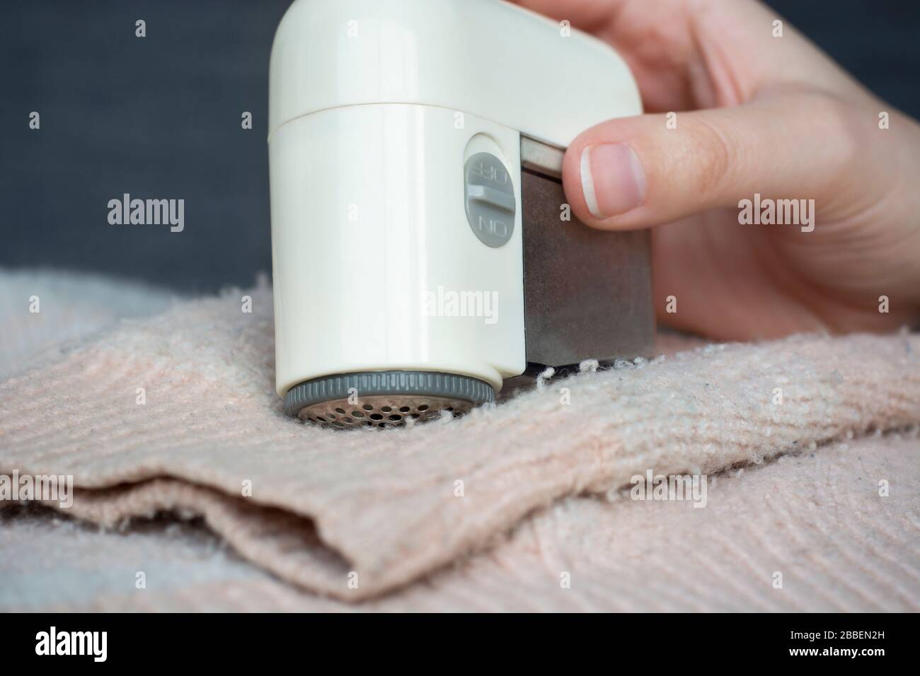 Maglione pillato. Donna mano che usa il dispositivo di rimozione del fuzz del rasoio elettrico del tessuto portatile per rimuovere il fuzz, il pelucchi e le pillole (pallini) sui vestiti Foto Stock