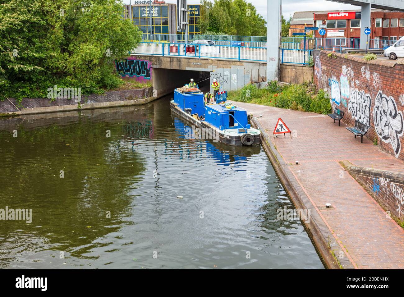 I lavoratori con un Canal e River Trust Barge effettuano riparazioni sul percorso di traino, Birmingham e Fazeley CANL, West Midlands, Regno Unito Foto Stock