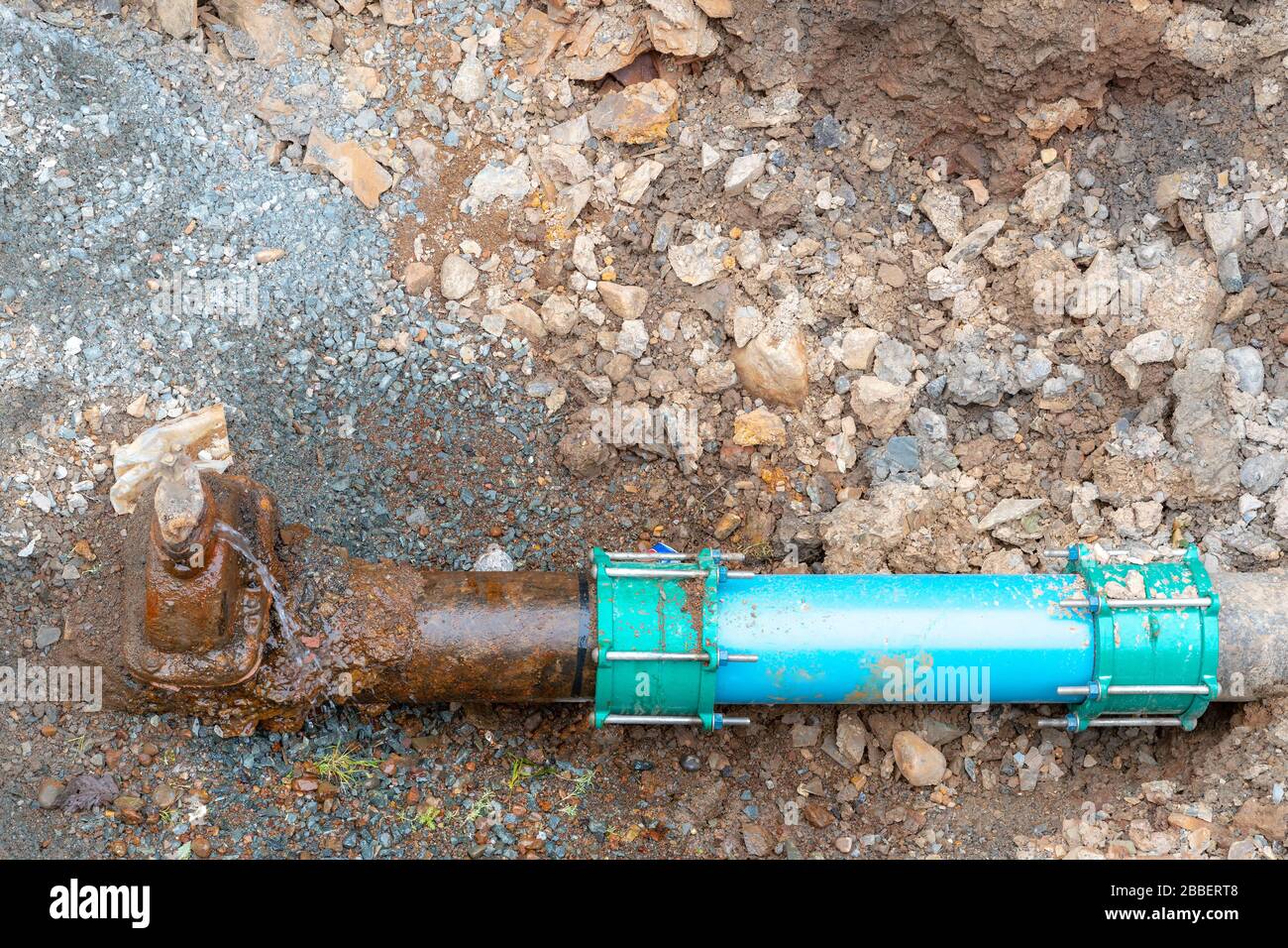 Un tubo di acqua comunale molto vecchio collegato ad un tubo nuovo. I tubi sono in sporco e ghiaia sul fondo di un foro. Il vecchio tubo perde da una ruggine Foto Stock