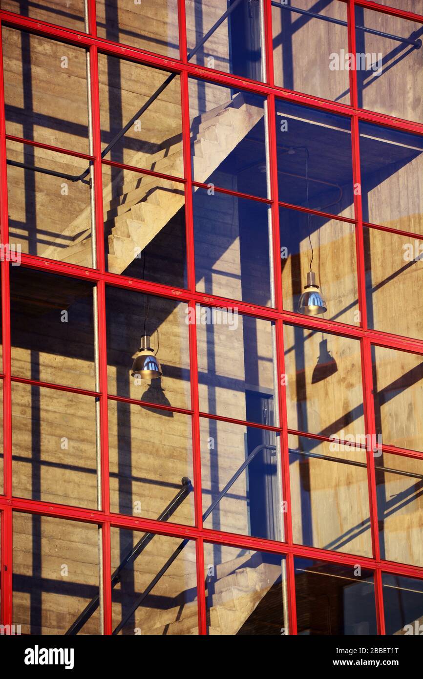 Scala con esterno in vetro nel pomeriggio sole gettando ombre sulle pareti in cemento provenienti dai telai in acciaio rosso delle finestre e appendere Foto Stock