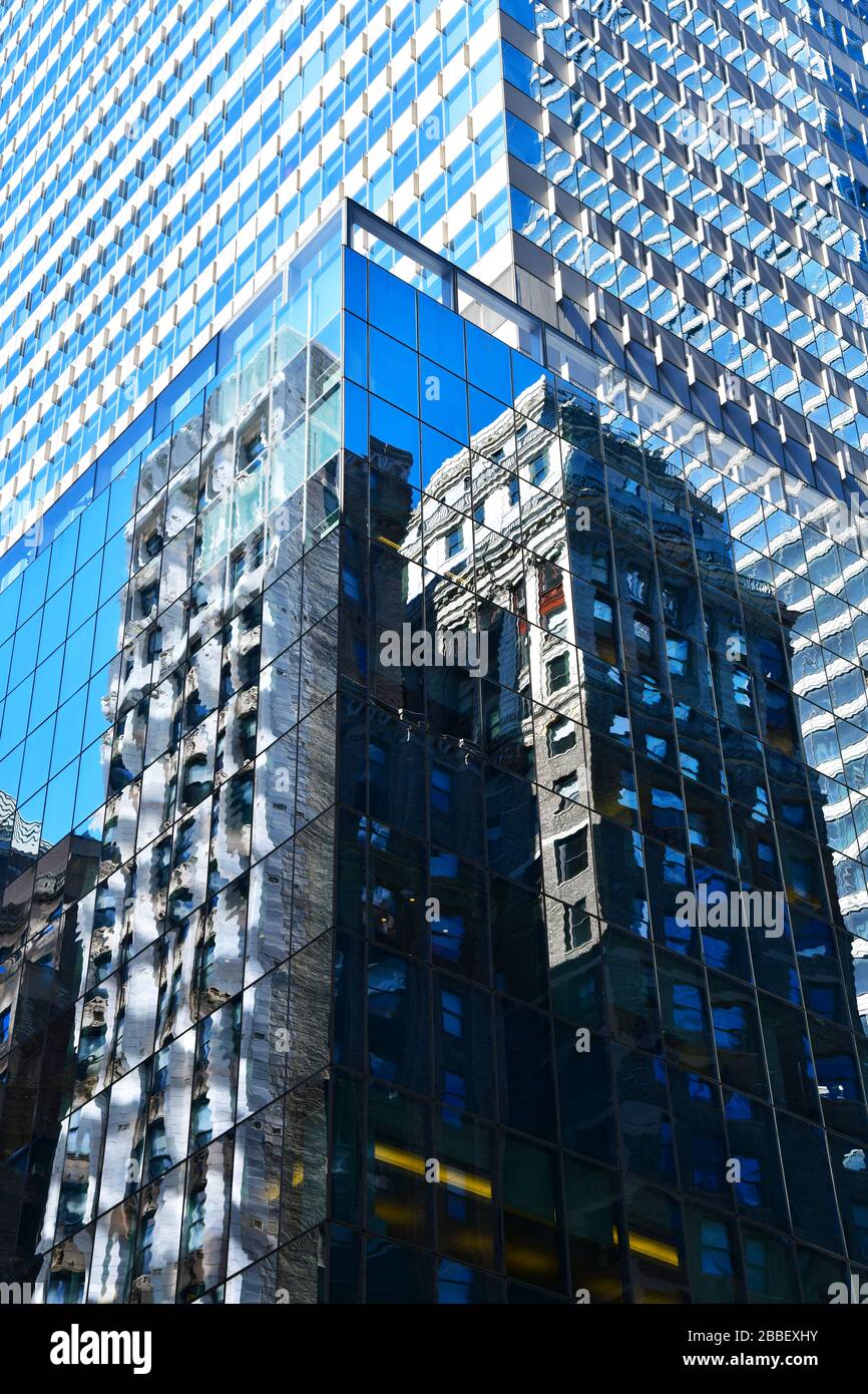 New York City, USA; vista a basso angolo e immagine che riempie moderno edificio in vetro con il riflesso di un edificio in mattoni marroni; quasi astratto Foto Stock