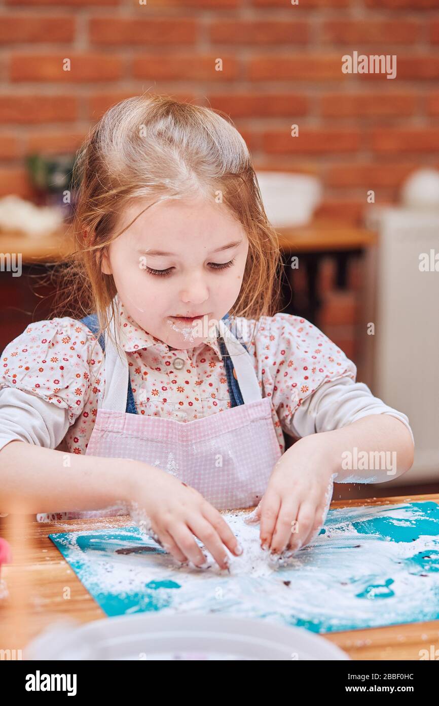 Bambina che mangia lo zucchero a velo lasciato dopo aver fatto cuocere i biscotti. Capretto che partecipa al laboratorio di cottura. Lezioni di cottura per bambini, aspiranti piccoli chef. Foto Stock