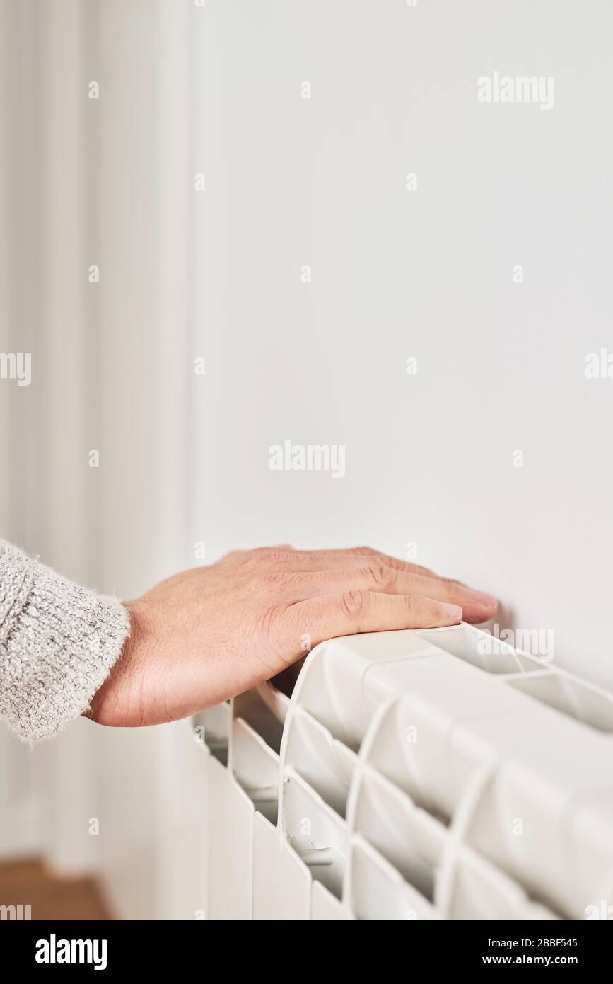 primo piano di un uomo caucasico, con un maglione grigio chiaro, toccando un radiatore ad acqua calda per controllarne la temperatura o riscaldare la mano Foto Stock